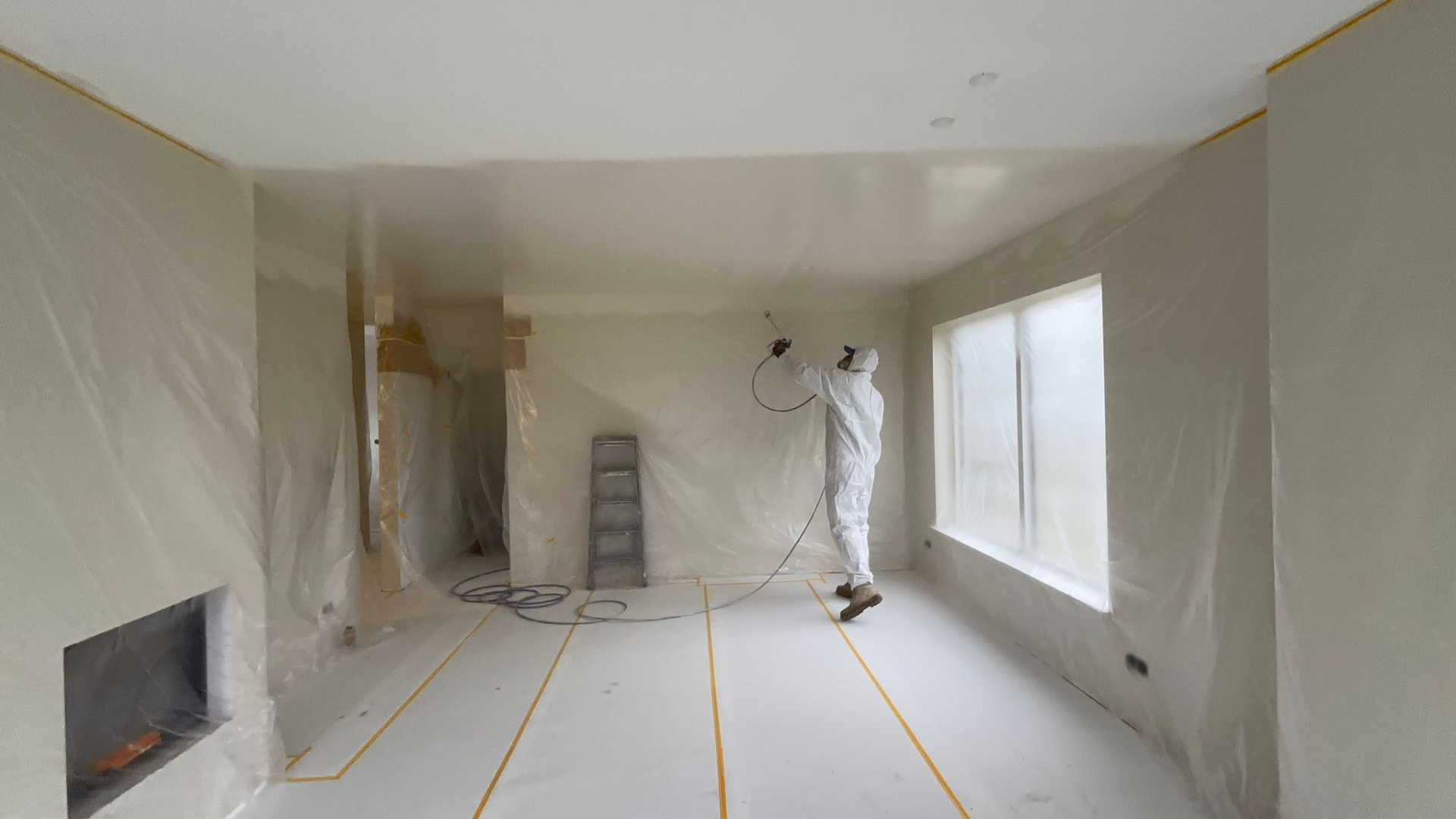 Medewerker in beschermende kleding spuit het plafond in een volledig afgeplakte ruimte